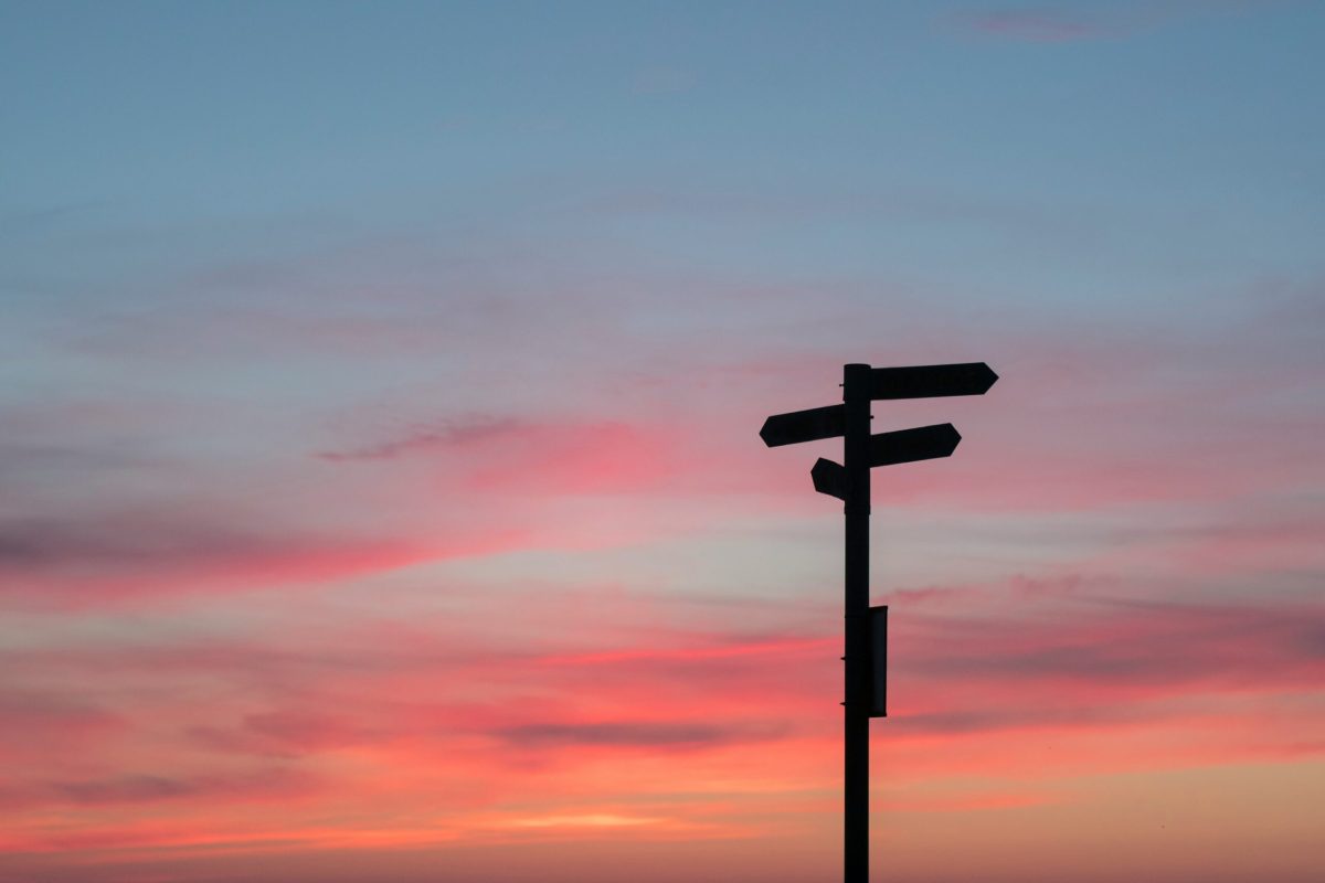 A multi-directional signpost silhouetted against a pink and blue sunset sky