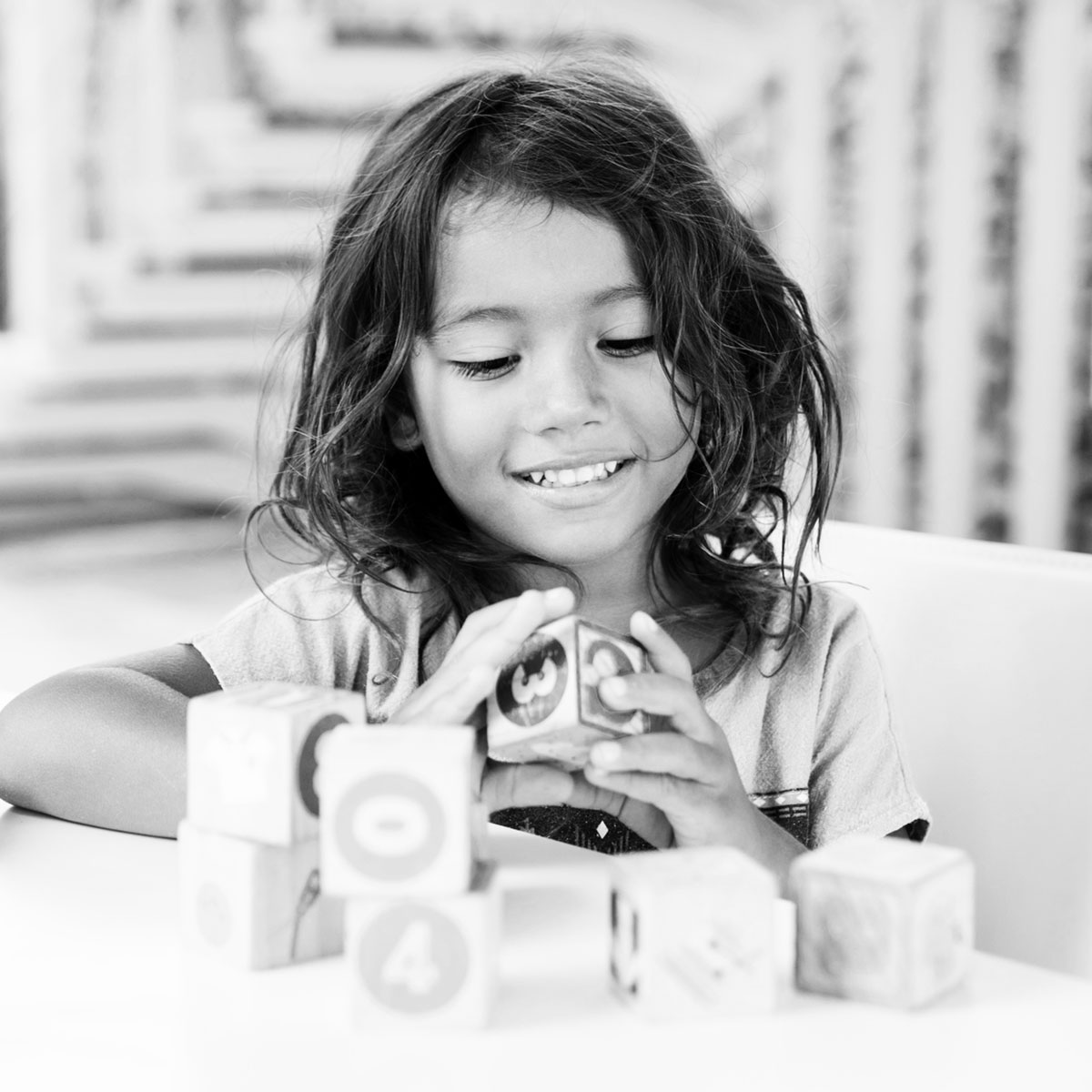 A young child smiling while playing with wooden number blocks